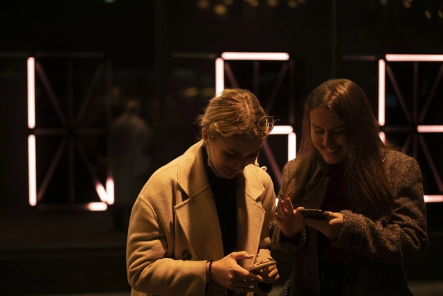 Zwei Besucherinnen schauen auf ihr Smartphone vor der Lichtinstallation.